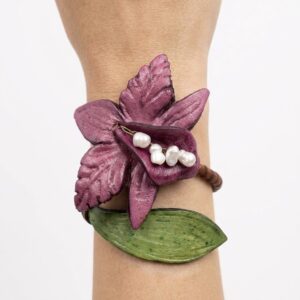 Brazalete artesanal con forma de orquídea lila y hoja verde con detalle de perlas centrales sobre fondo blanco.
