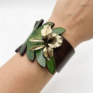 Brazalete de cuero verde y marrón con detalle de orquídea en metal oro viejo sobre fondo blanco